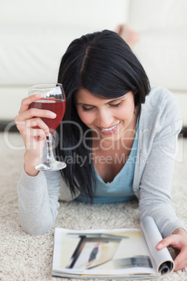 Woman holding a glass of wine and smiling while reading a magazi