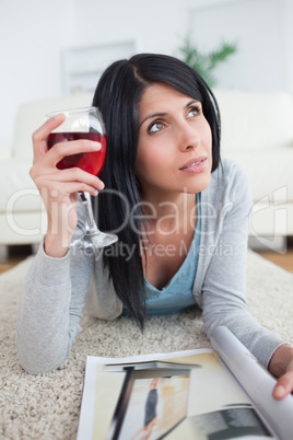 Woman thinking while holding a glass of red wine and a magazine