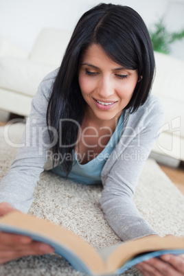 Smiling woman reading a book while lying on the floor