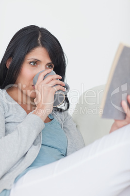 Woman reading a book while drinking a from a mug