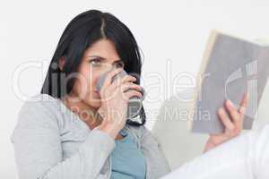 Woman drinking a mug while reading a book