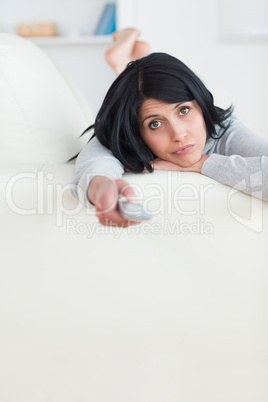 Woman pressing on a remote control while lying on a couch