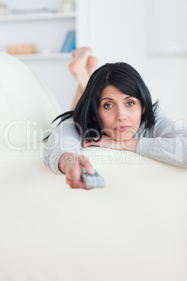 Woman pressing on a television remote while laying on a sofa