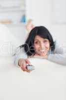 Woman pressing on a remote control while laying on a sofa