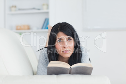 Woman holding a book while laying on a sofa