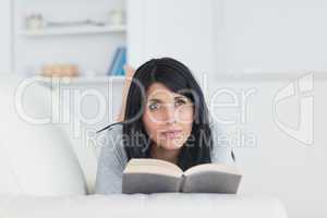 Woman holding a book while laying on a sofa