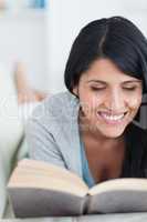 Woman smiling while reading a book as she lies on a couch