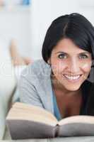 Smiling woman reading a book as she lies on a sofa