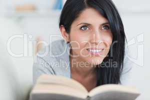 Woman smiling while holding a book and lying on a couch
