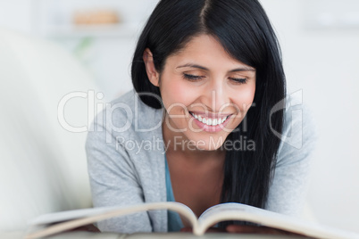 Woman reading a book and smiles as she lies on a couch