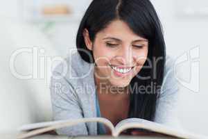 Woman reading a book and smiles as she lies on a couch