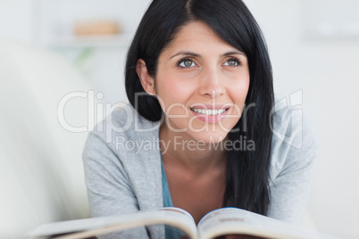 Woman smiling while holding a book and laying on a sofa