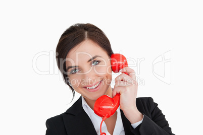 Smiling woman in suit using a red dial telephone
