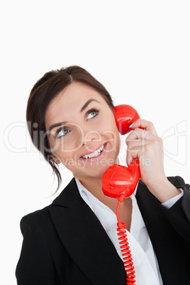 Happy woman in suit using a red dial telephone while looking up