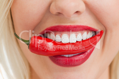 Happy blonde woman holding a chili with her mouth