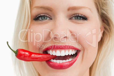 Happy blonde woman biting a red chili pepper