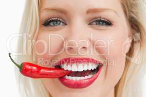 Happy blonde woman biting a red chili pepper