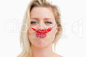 Blonde woman placing a chili between her nose and her mouth