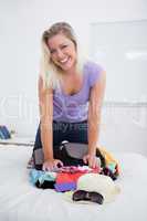 Blonde laughing while trying to close her luggage