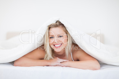 Young blonde woman lying under a duvet