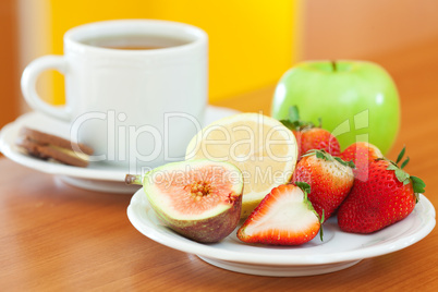 cup of tea,cookie,apple, lemon, fig and strawberries on a plate