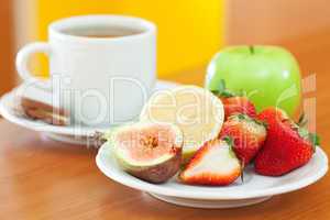 cup of tea,cookie,apple, lemon, fig and strawberries on a plate