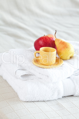 cup,apple and pear on towels on the bed