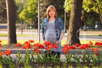 Pregnant woman standing near flowerbed