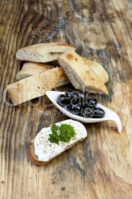 Grüne Oliven mit frischem Brot und Kräutern auf einem Holzbret