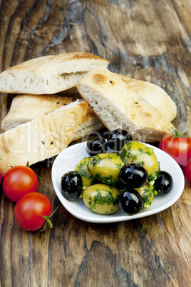 Grüne Oliven mit frischem Brot und Kräutern auf einem Holzbret