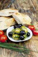 Grüne Oliven mit frischem Brot und Kräutern auf einem Holzbret