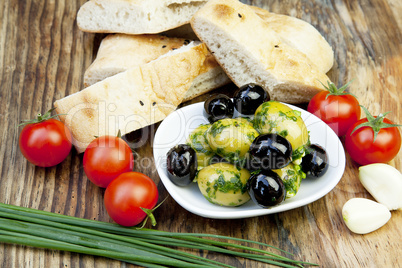 Grüne Oliven mit frischem Brot und Kräutern auf einem Holzbret