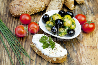 Grüne Oliven mit frischem Brot und Kräutern auf einem Holzbret