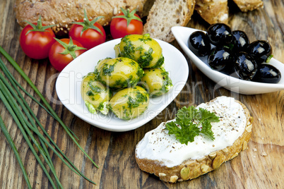 Grüne Oliven mit frischem Brot und Kräutern auf einem Holzbret