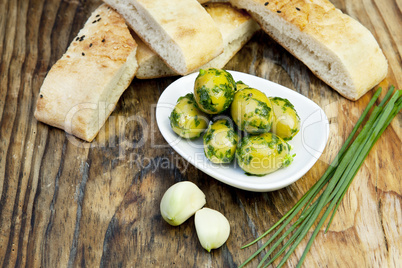 Grüne Oliven mit frischem Brot und Kräutern auf einem Holzbret