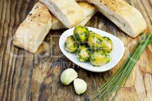 Grüne Oliven mit frischem Brot und Kräutern auf einem Holzbret
