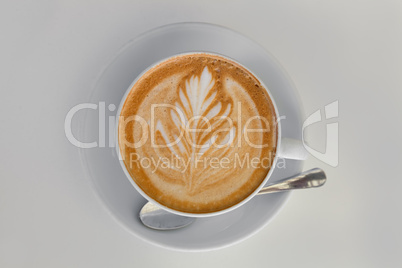 Cappucino with leaf shape foam on white saucer with spoon
