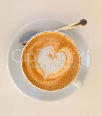 Cappucino with heart shape foam on white saucer with spoon