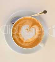 Cappucino with heart shape foam on white saucer with spoon