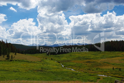 High green plateau with stream, forests, mountains and beautiful clouds, Wyoming