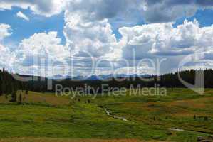 High green plateau with stream, forests, mountains and beautiful clouds, Wyoming