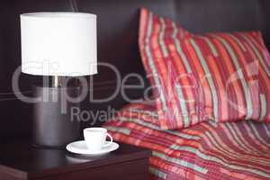 bed with a pillow, a cup of tea on the bedside table and lamp