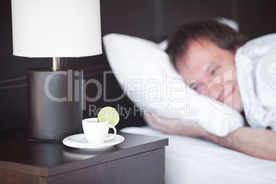 man sleeping on a bed, a cup of tea on the bedside table and lam