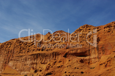 Holes in orange rock wall under blue skies on Burr Trail Road, Utah