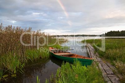 Summer's lake scenery with wooden boat and rainbow