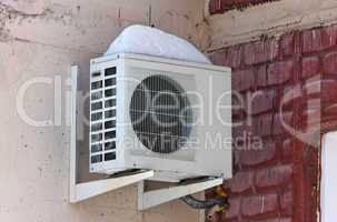 Air conditioning heat pump mounted on brick wall.