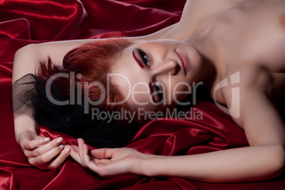 Nude young woman lying on red sheet