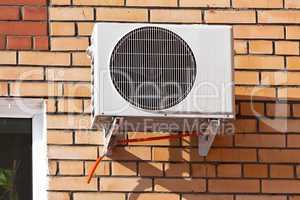 Air conditioning heat pump mounted on brick wall.