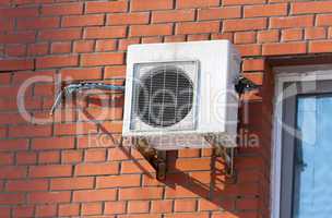 Air conditioning heat pump mounted on brick wall.