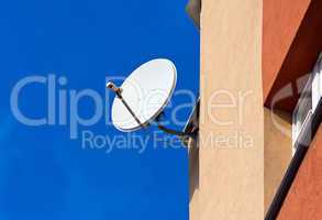 Satellite Dish mounted on  brick wall against blue sky backgroun